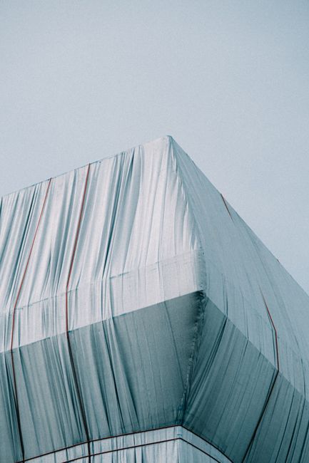 A minimalistic architectural detail of a building corner wrapped in white fabric against a clear sky.