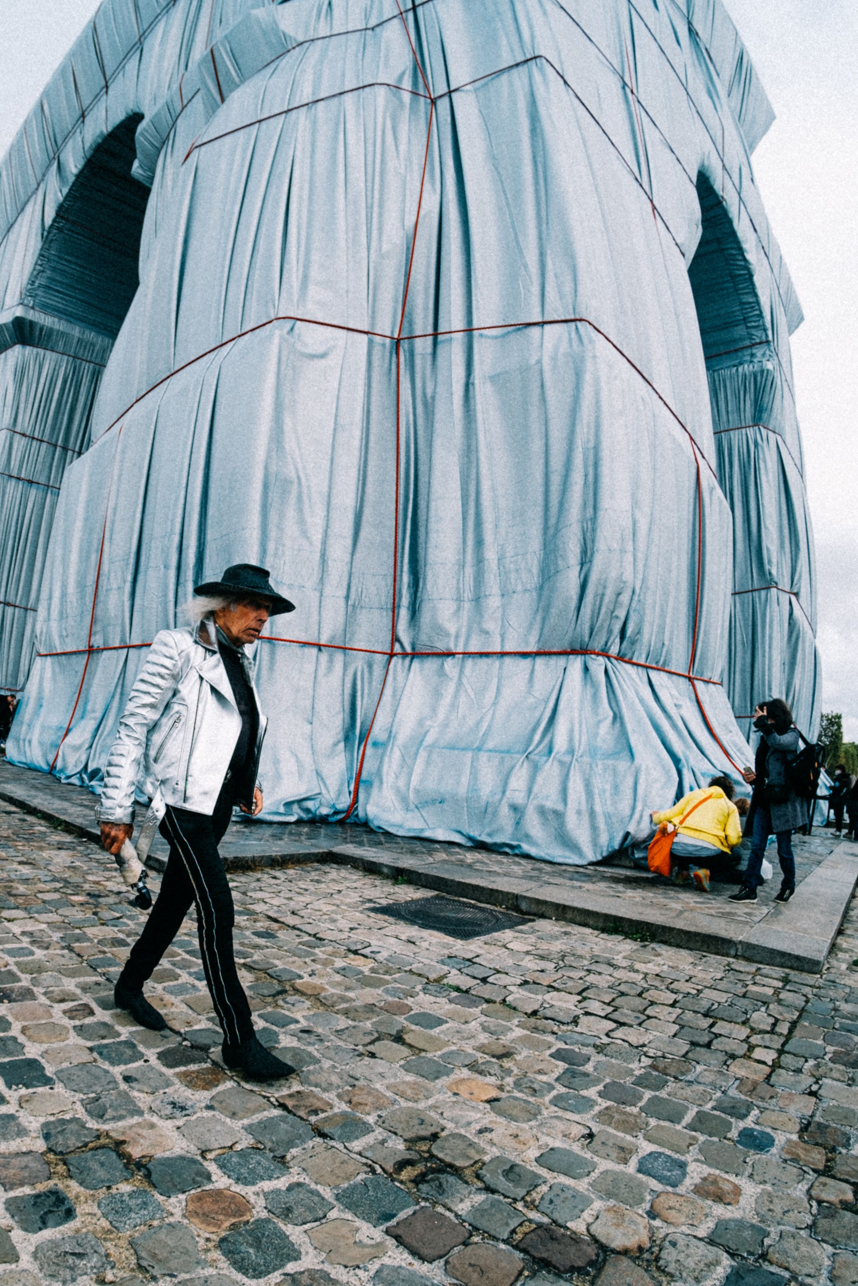 The Arc de Triomphe in Paris wrapped for an art installation, with people walking nearby.