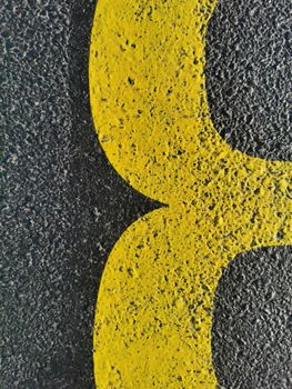 Detailed view of a yellow road marking on rough asphalt surface. Urban texture concept.