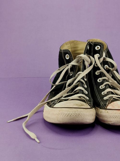 Free Pair of worn black sneakers with shoelaces on a purple background. Classic fashion footwear. Stock Photo
