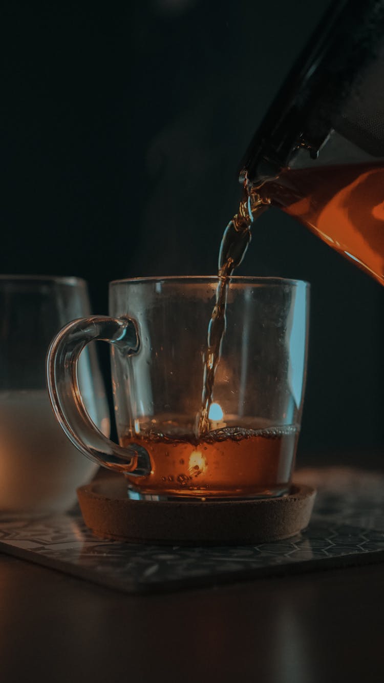 A Person Pouring A Tea On A Clear Glass Mug