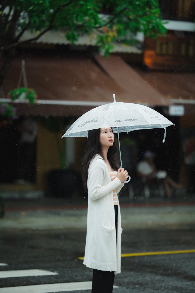 A Woman Crossing The Road While Holding An Umbrella