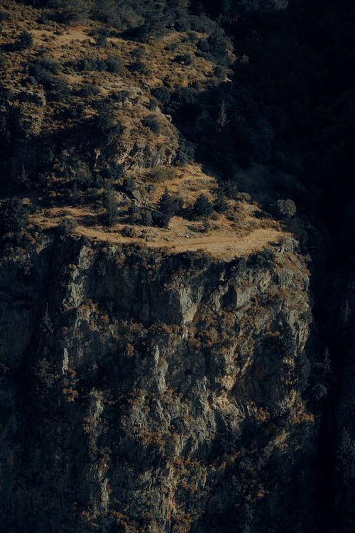 Free Captivating view of a rugged rocky cliff with vegetation under natural light. Ideal for nature themes. Stock Photo
