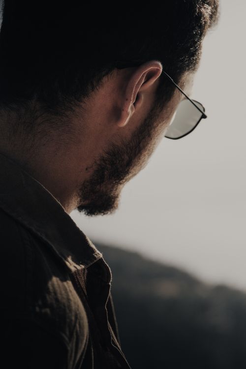 Free A thoughtful man viewed from behind, wearing sunglasses in soft lighting, creating a moody atmosphere. Stock Photo