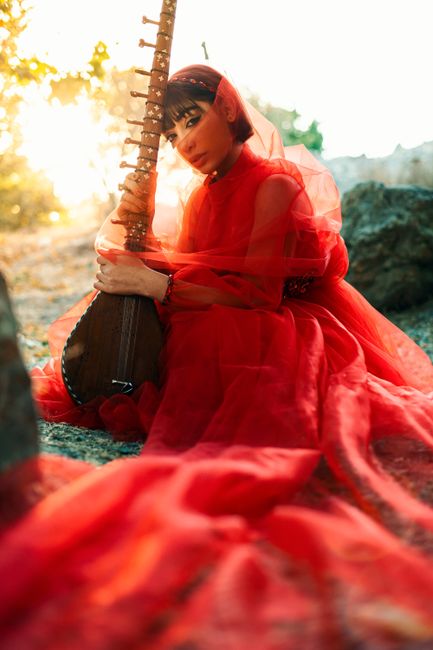 Captivating image of a woman in a red dress sitting with a traditional Persian instrument, bathed in sunset light.