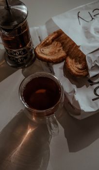 Warm black tea in a glass cup with croissants and French press, creating a cozy breakfast scene.