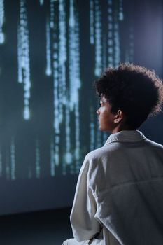 A teenager contemplates digital code projections in a dimly lit room, emphasizing technology and introspection.