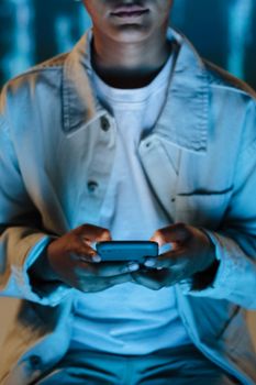 A person focused on a smartphone in a dimly lit indoor setting, highlighting technology use.