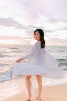 A happy woman in a white dress enjoying a breezy day on the beach at sunset.