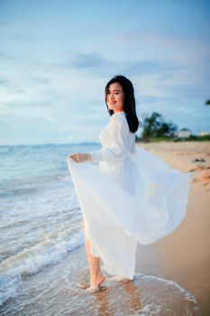 Serene beach scene with a woman in a white dress enjoying a seaside stroll at sunset.
