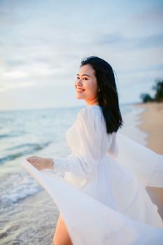 A smiling woman in a white dress enjoys a peaceful beach at sunset, capturing a moment of joy and tranquility.