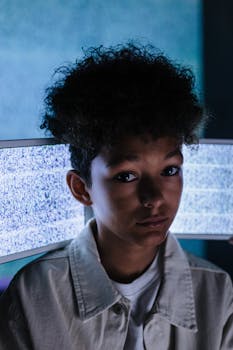 Moody portrait of a teenager in front of static TV screens with blue lighting.