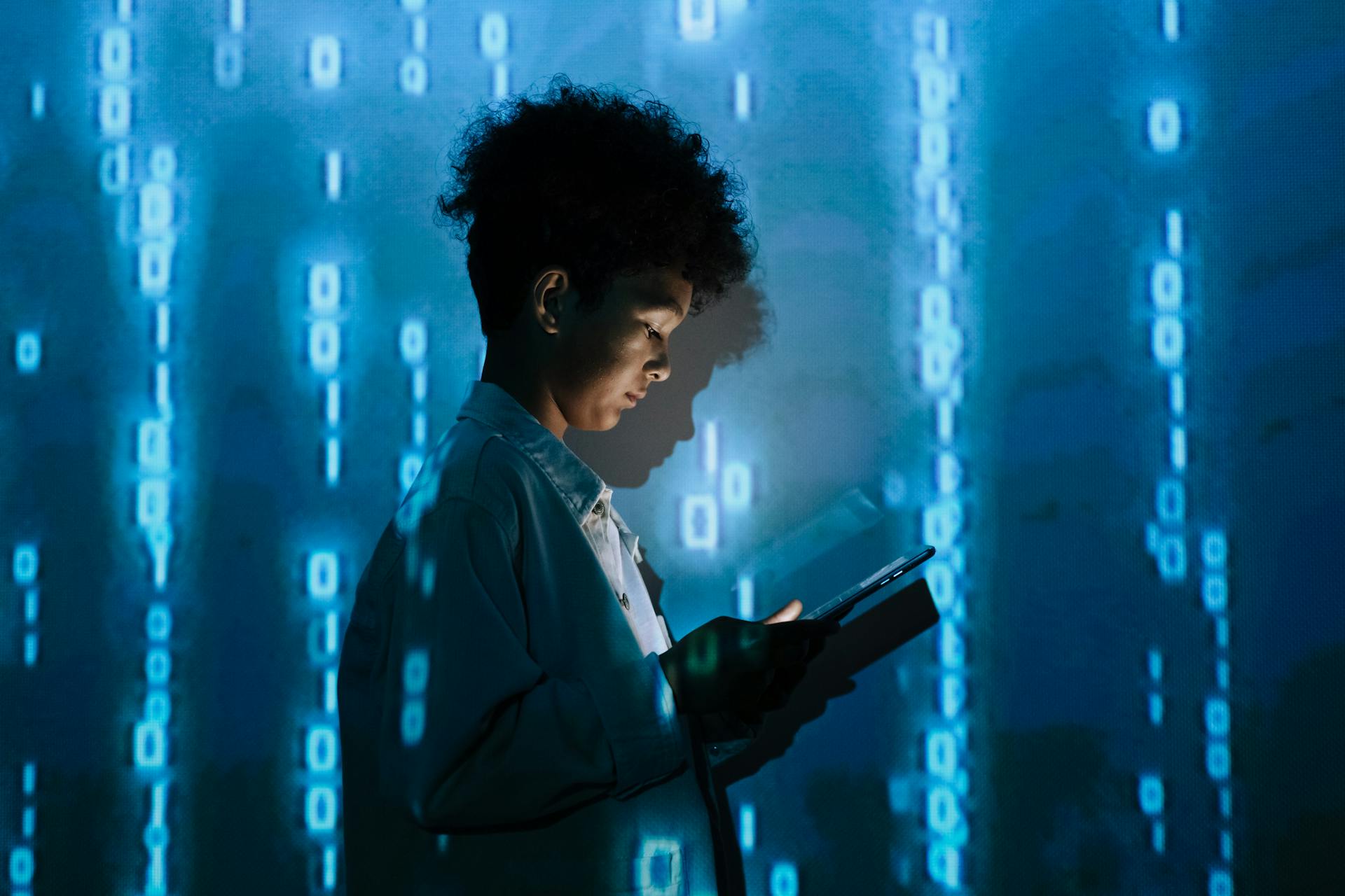 Teenage boy with a tablet surrounded by digital binary code in a studio setting.