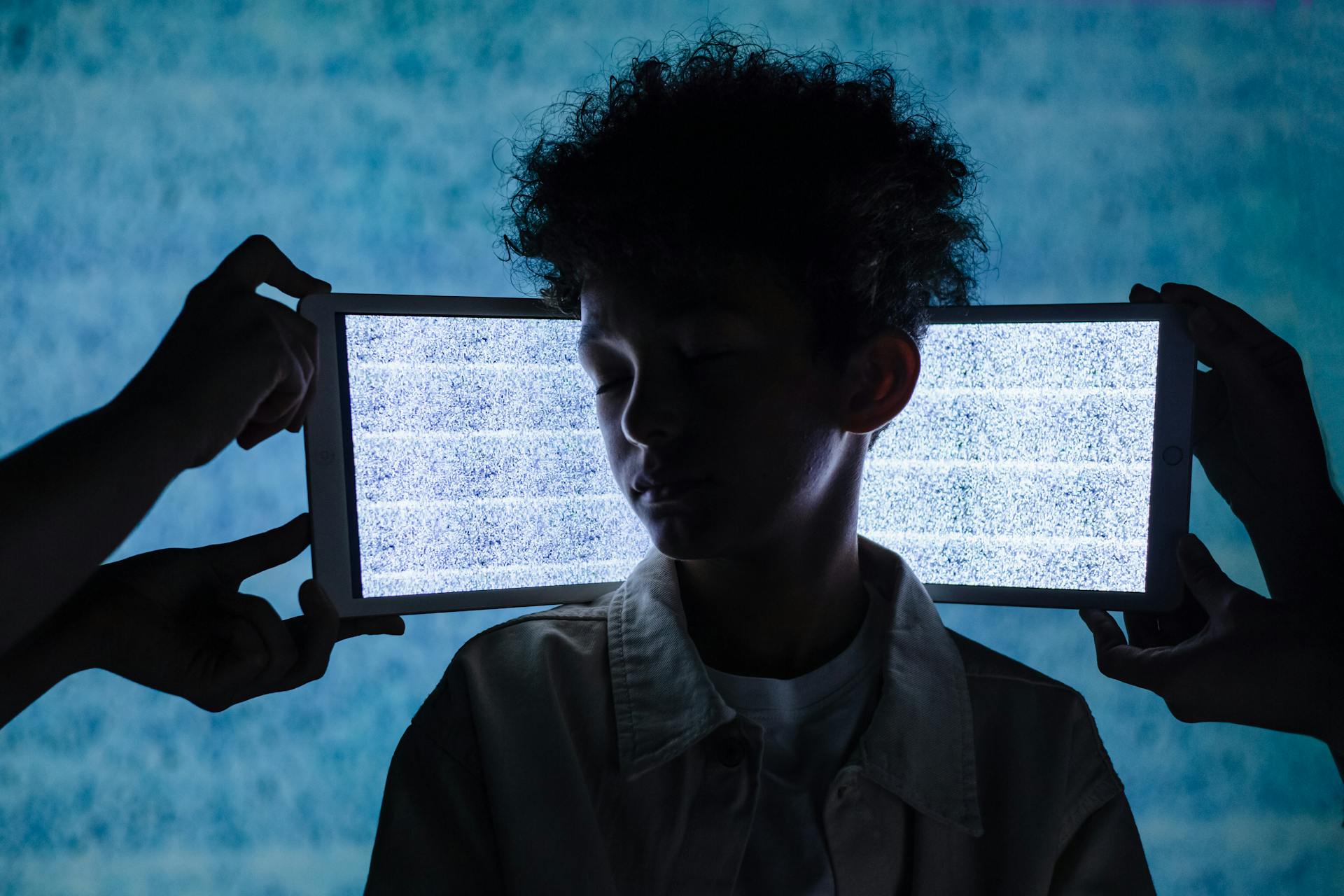 Two iPad Screens Behind Boy with Closed Eyes