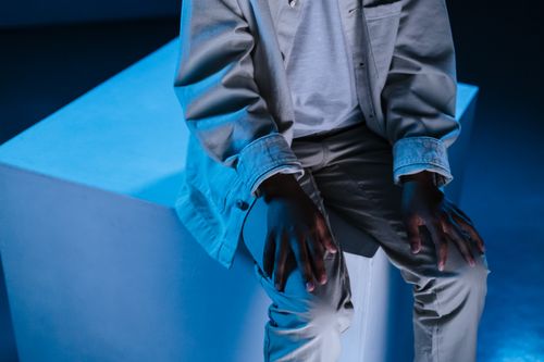 Free Close-up of a person sitting on a blue-tinted cube, focusing on hands and attire. Stock Photo