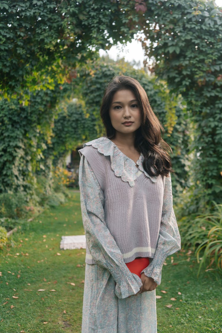 A Young Woman Holding A Book While Standing In A Garden