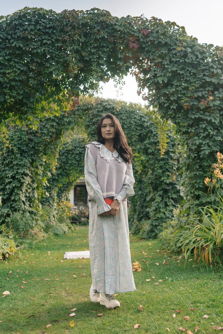 A Young Woman Holding A Book While Standing In A Garden