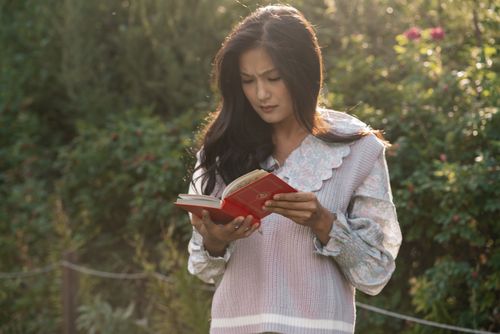 Free Woman in a floral top reading a book in a lush garden during the day. Stock Photo