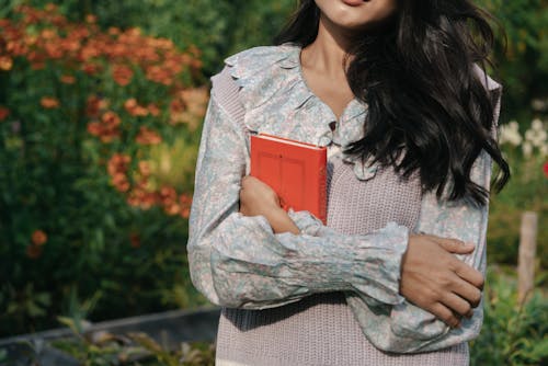 Woman in Floral Top and Knit Vest Holding a Book