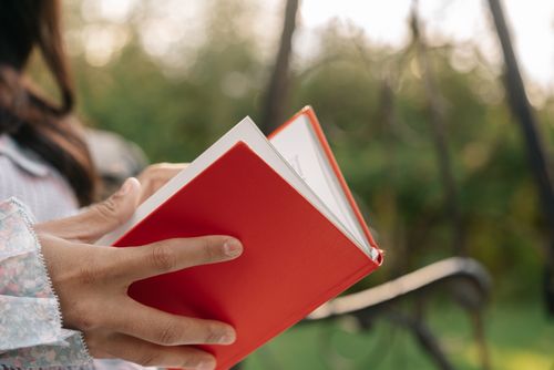 Free A woman enjoys reading a red book outdoors. Focus on hands and book. Stock Photo