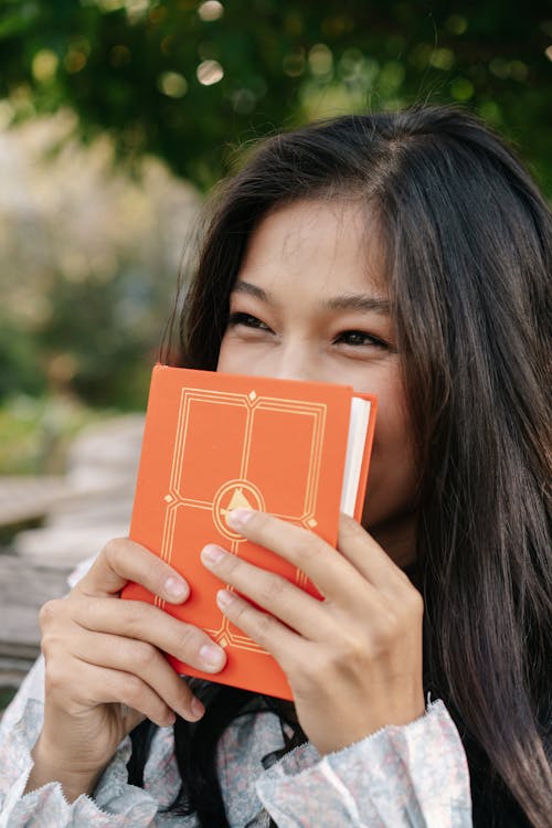 Woman Covering Her Face with an Orange Book