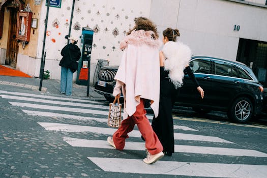 Stylish women walk across a city crosswalk showcasing modern fashion and accessories.