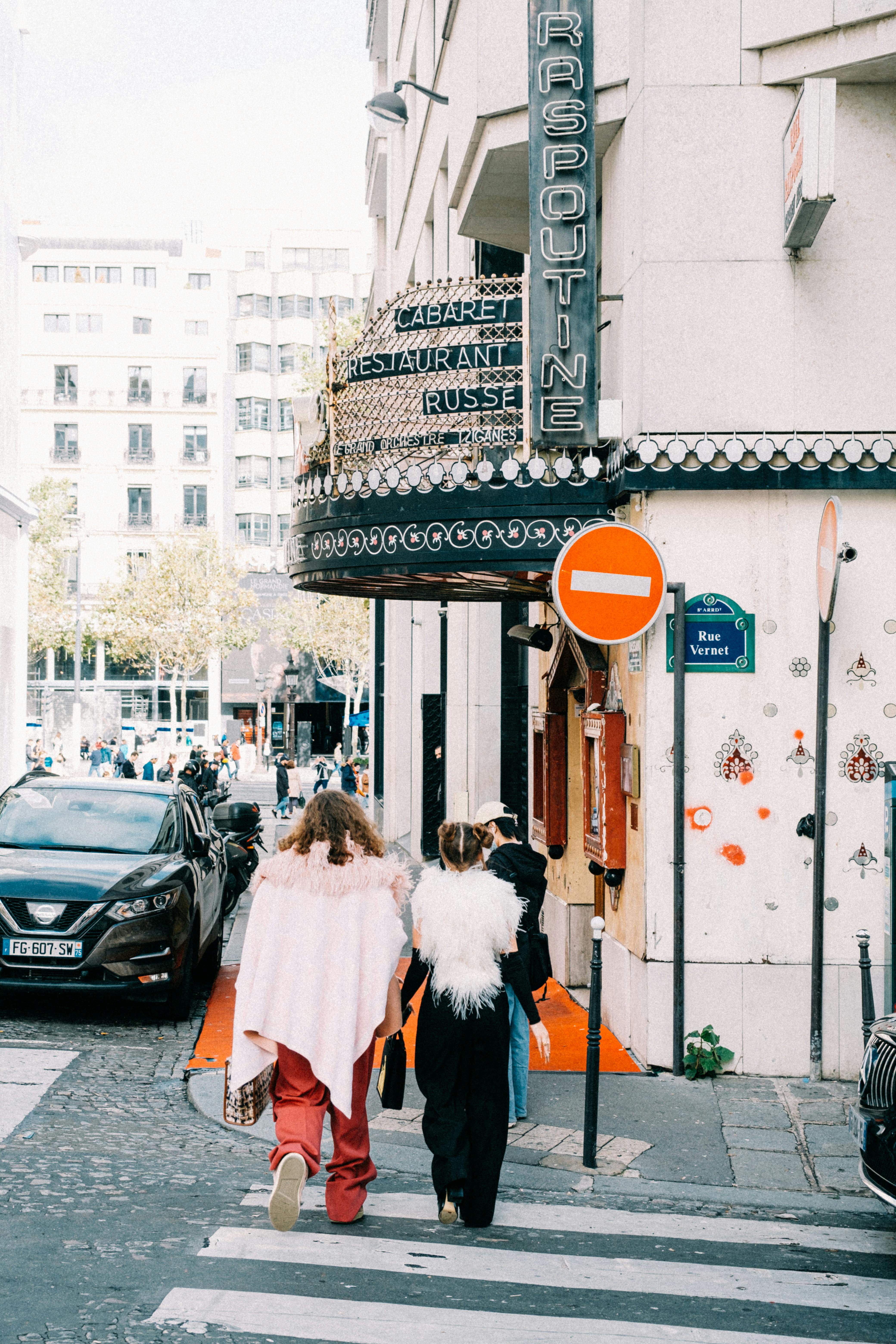 Free Two people in costumes walking past a Russian cabaret in a bustling city street. Stock Photo