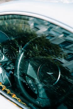 Interior view of a luxury car with reflections on the window showing steering wheel and dashboard.