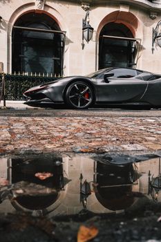 Black sports car with reflection on a cobblestone street beside a stylish building facade.