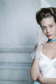 Portrait of a young woman in vintage fashion with lace gloves and feathered hat indoors.