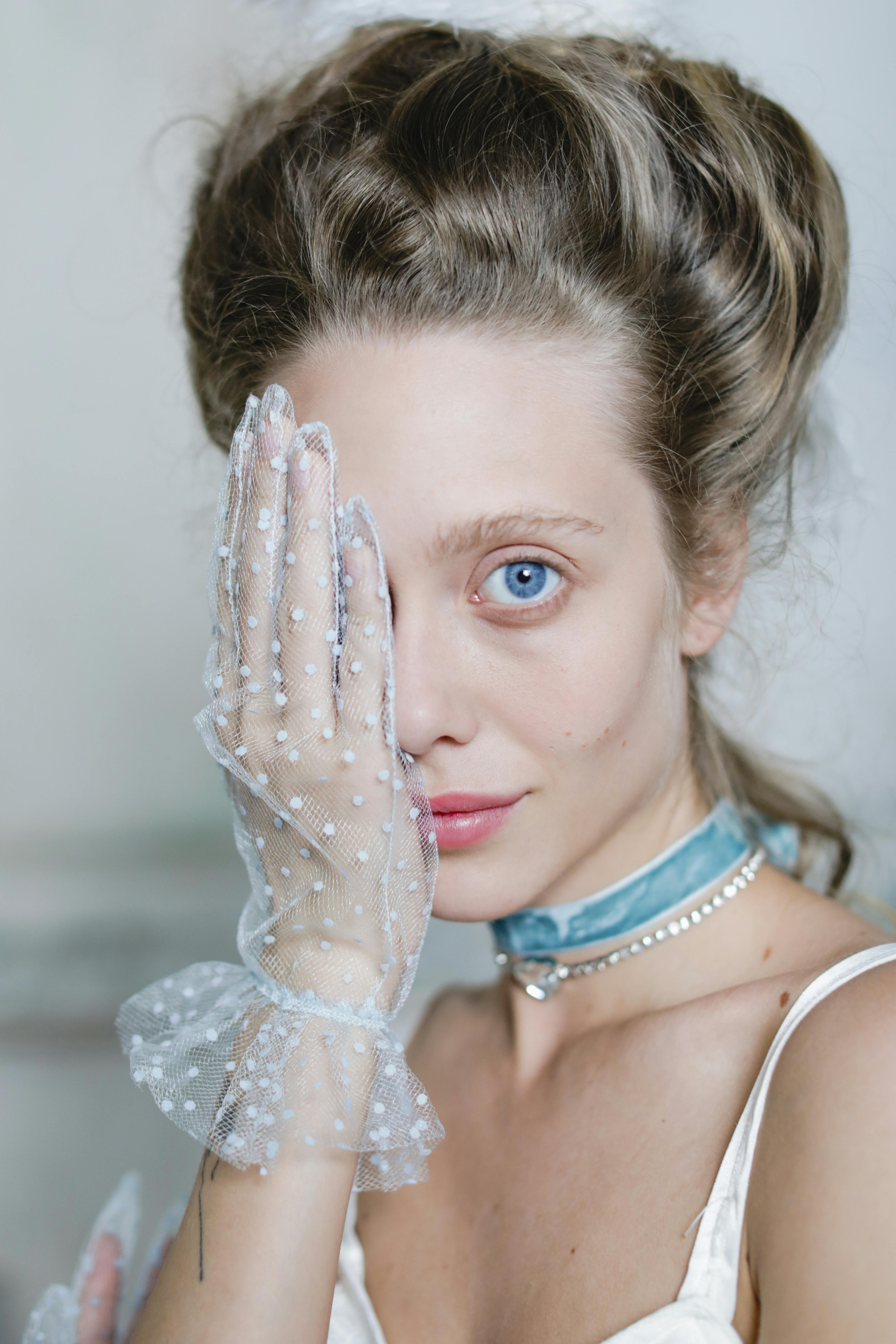 Portrait of a woman wearing lace gloves and a blue necklace, posing elegantly.