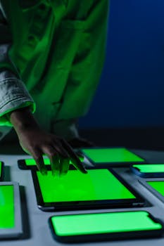 A hand interacts with multiple green screen electronic devices in a dimly lit room.