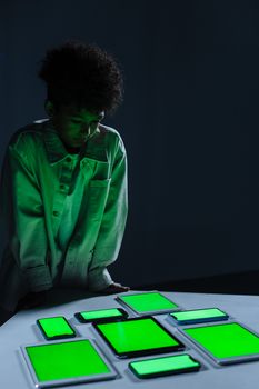 Young boy in a studio setting surrounded by multiple green screen digital devices depicting technology engagement.
