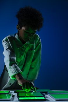 Young boy in a studio interacting with multiple digital screens, illuminated by green light.
