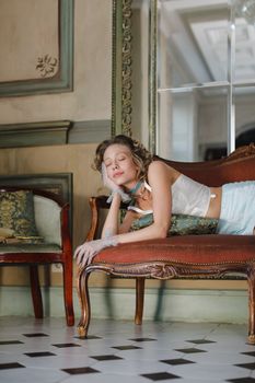 Elegant woman with closed eyes in vintage attire resting on a classic sofa, indoors.