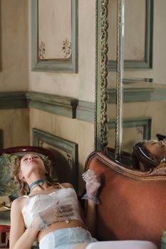 A woman in period-inspired lingerie poses elegantly in an ornate room.