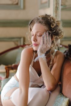 Chiffon-gloved woman in vintage lingerie, posing with eyes closed on a sofa.
