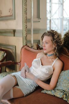 A young woman poses elegantly in vintage lingerie on a luxurious sofa.