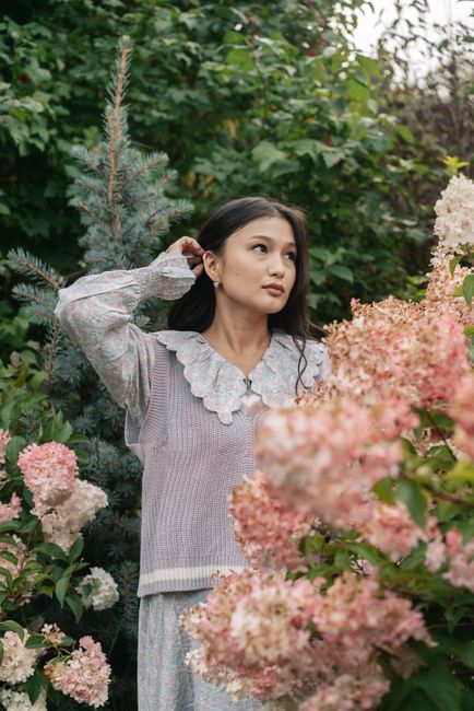 Young woman stands amidst blooming pink hydrangea garden, looking serene and thoughtful.