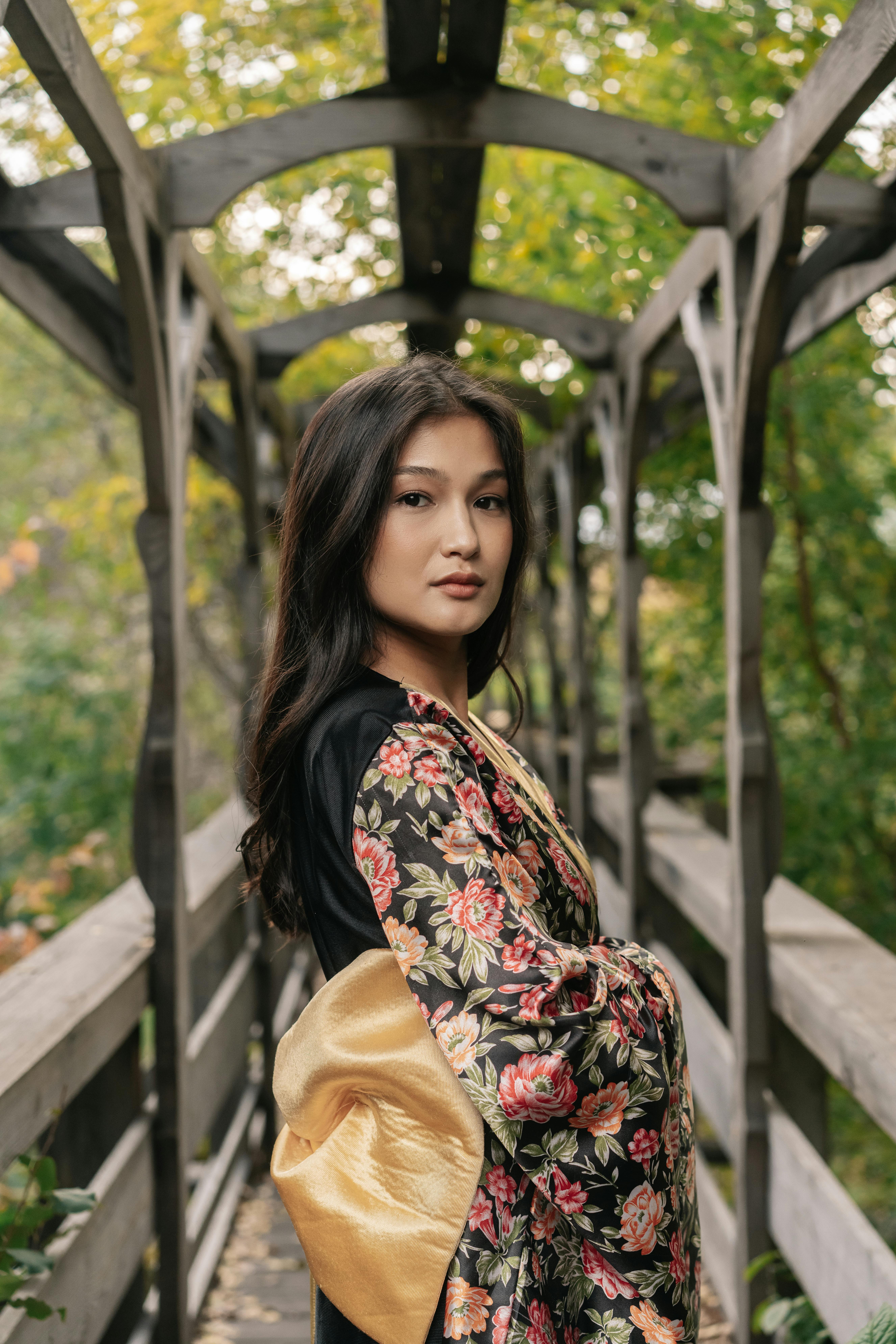 穿着传统花卉和服的亚洲妇女在郁郁葱葱的绿色植物包围的木桥上优雅地摆姿势