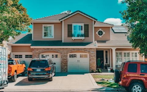 A suburban house with cars parked in the driveway on a sunny day