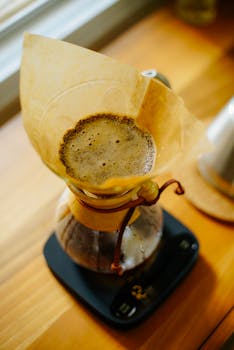 High-angle view of a Chemex coffee maker brewing fresh coffee on a wooden surface, emphasizing artisanal preparation.