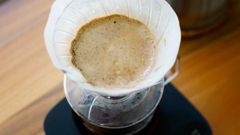 Overhead view of pour-over coffee brewing with kettle and scale on a wooden surface.