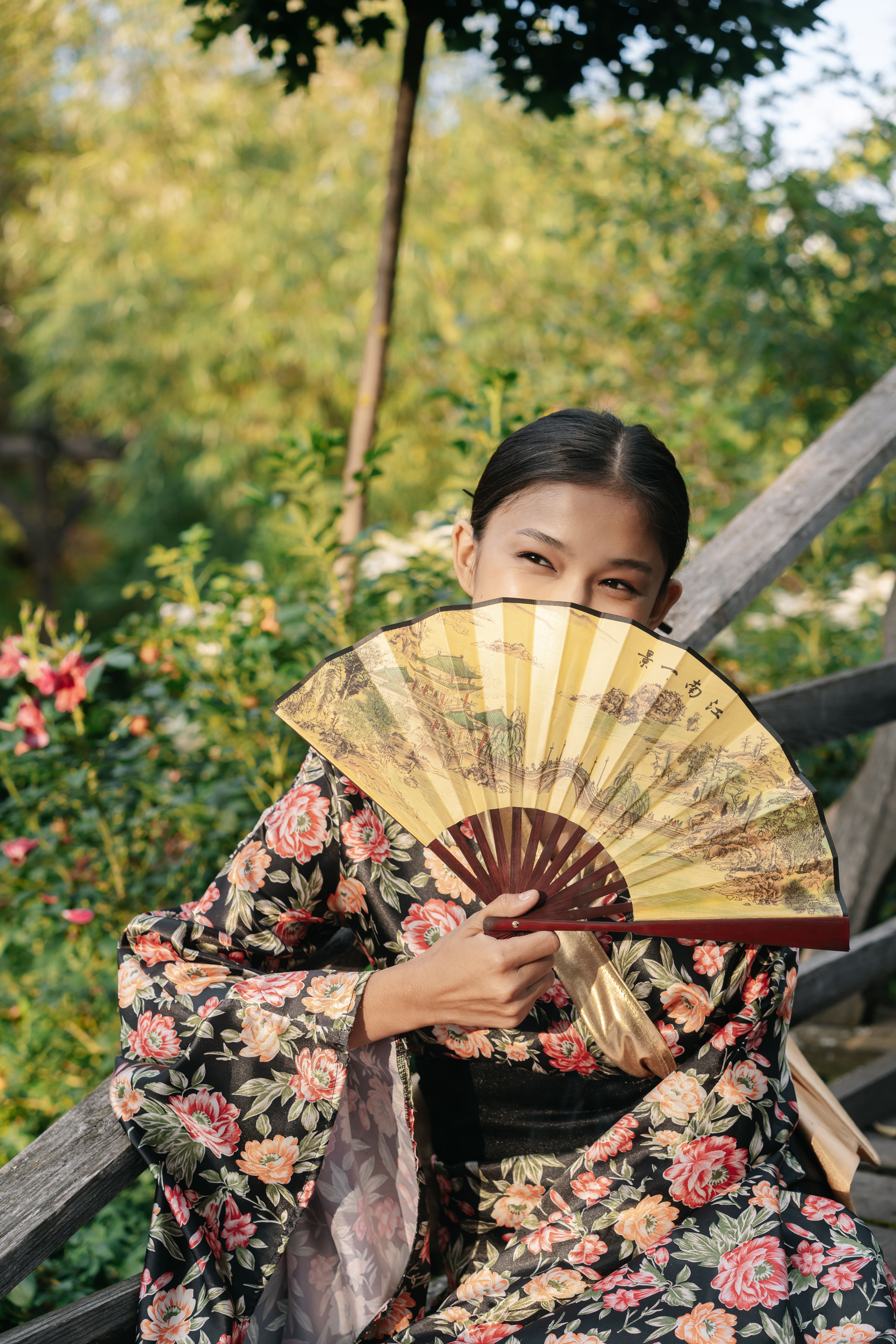 Charming young woman in traditional Japanese kimono, holding a fan outdoors.