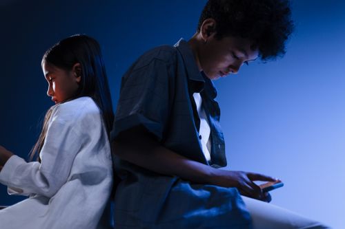 Free Young boy and girl using mobile devices in a conceptual studio setting with blue lighting. Stock Photo