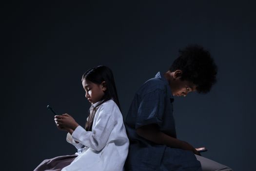 Two children focused on smartphones sitting back-to-back in a studio setting.