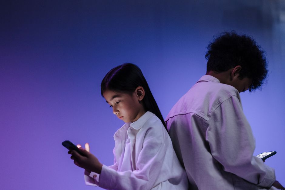 Dos niños usando smartphones de espaldas bajo luces coloridas de estudio.