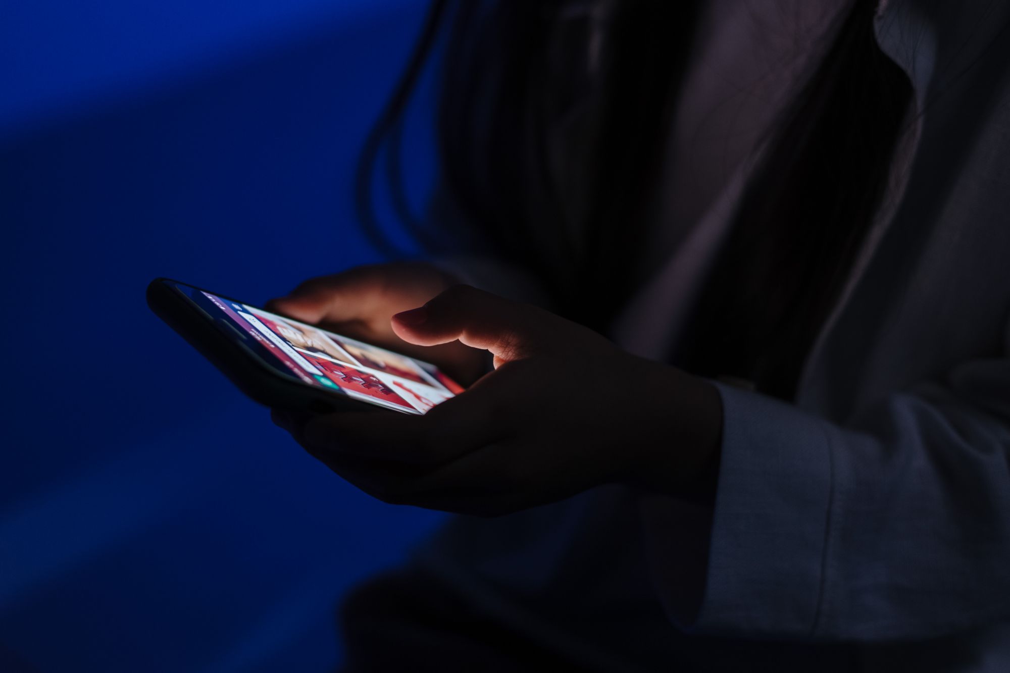 A teenager browses a smartphone in a dimly lit room, highlighting technology use.