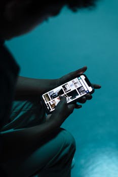 A person scrolling through images on a smartphone in a low-light setting.