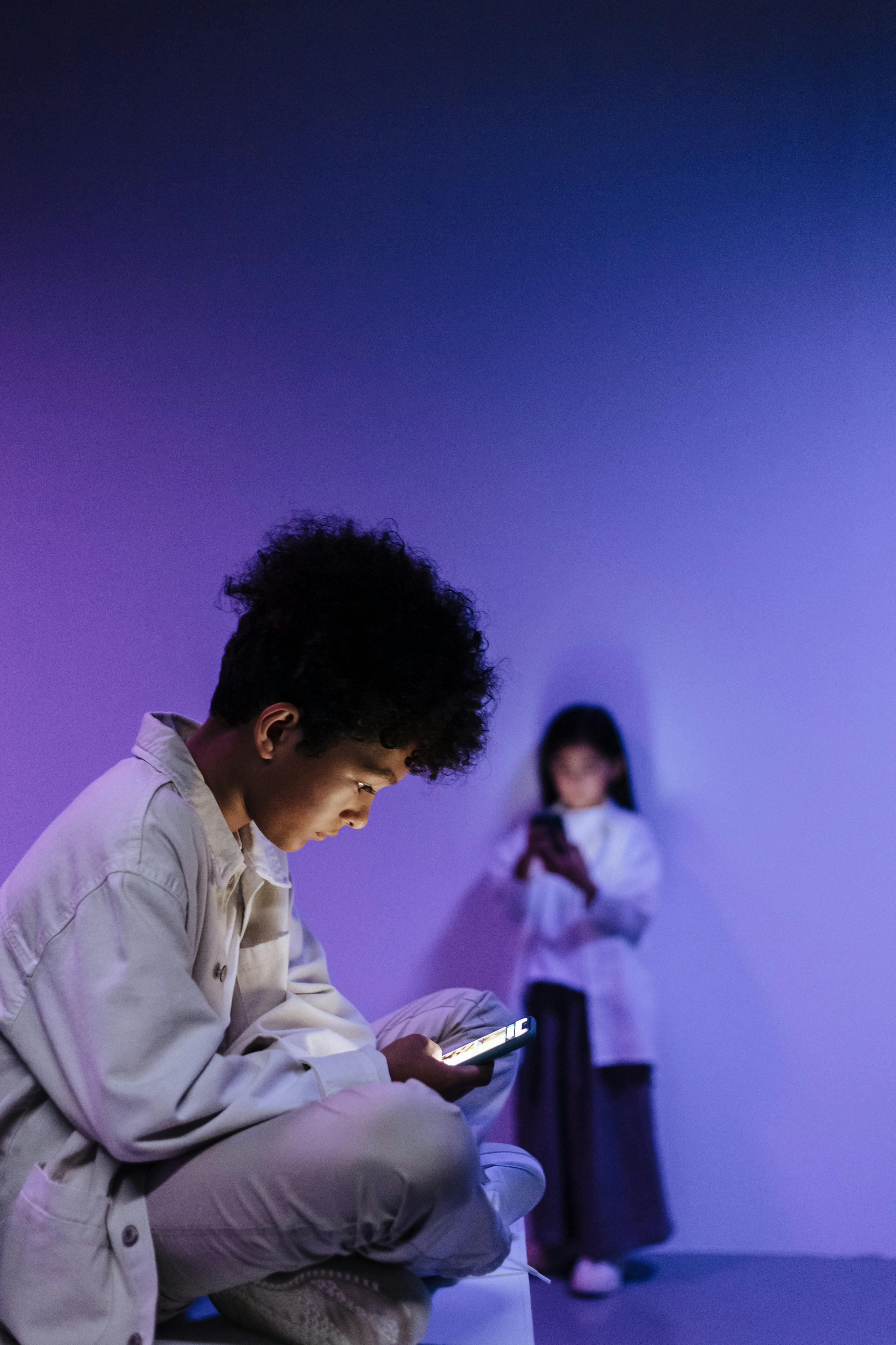 Two children with smartphones in a modern studio with colored lighting.
